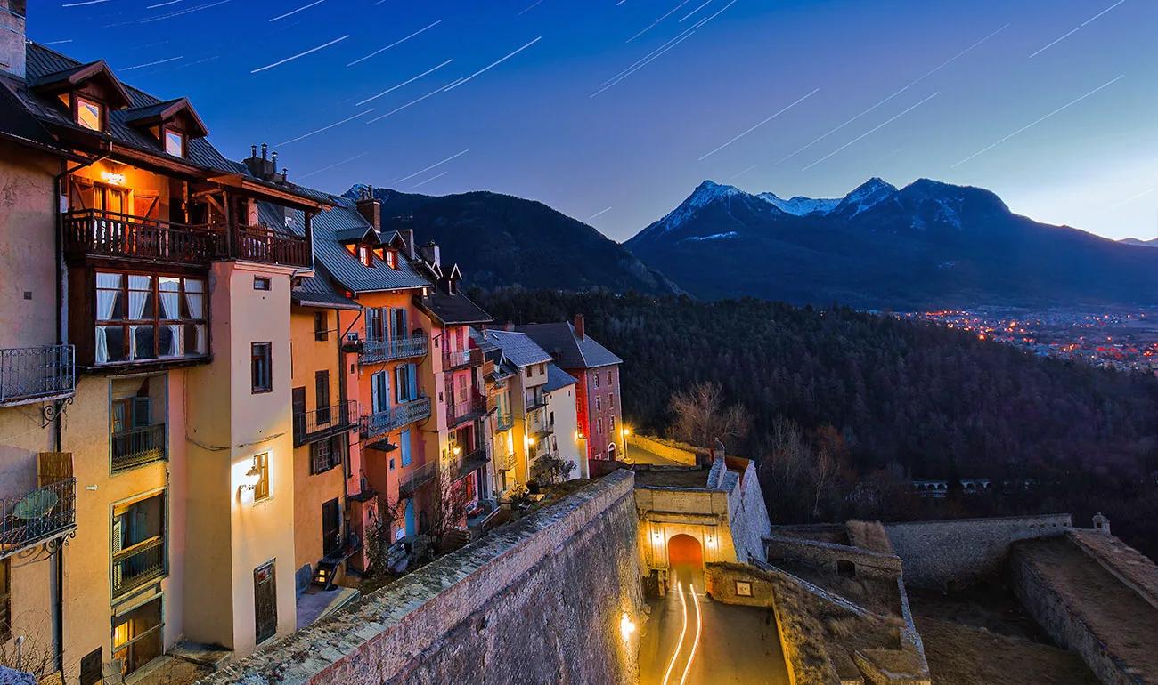 Briançon’s hillside rooftops lit up against the mountains at dusk
