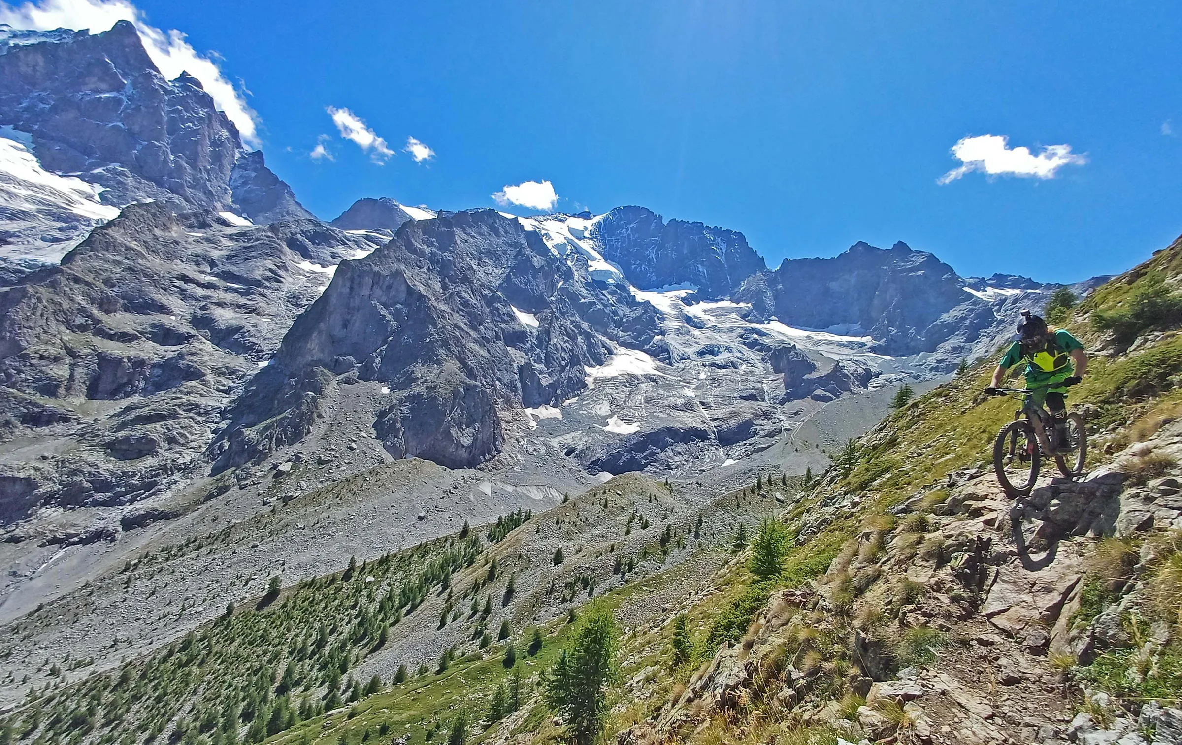 Mountain biker on a rocky Alpine trail beneath dramatic peaks and glaciers