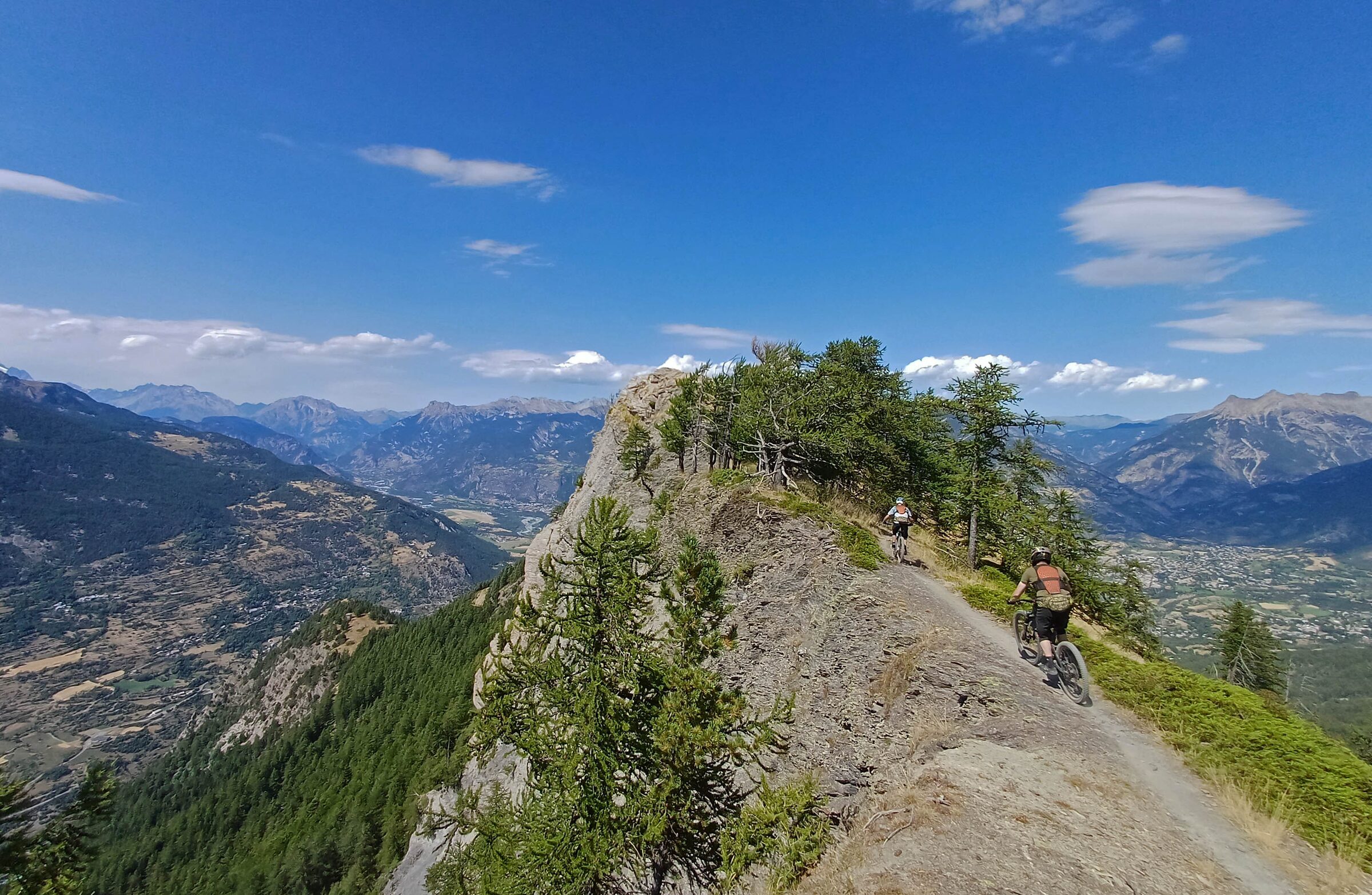 Two mountain bikers riding a rocky ridge trail high above an Alpine valley