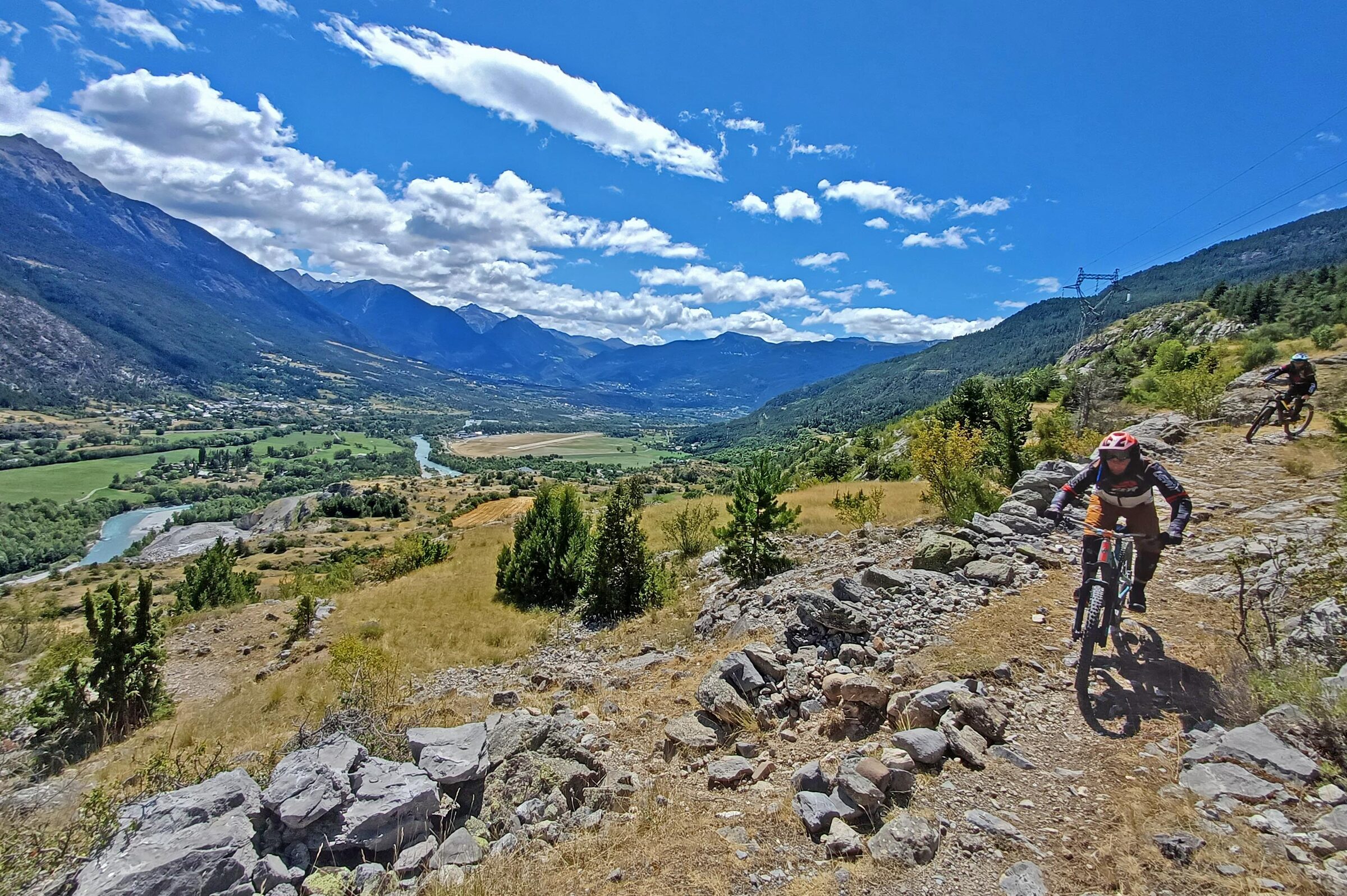 Two mountain bikers descending a rocky Alpine trail above the valley