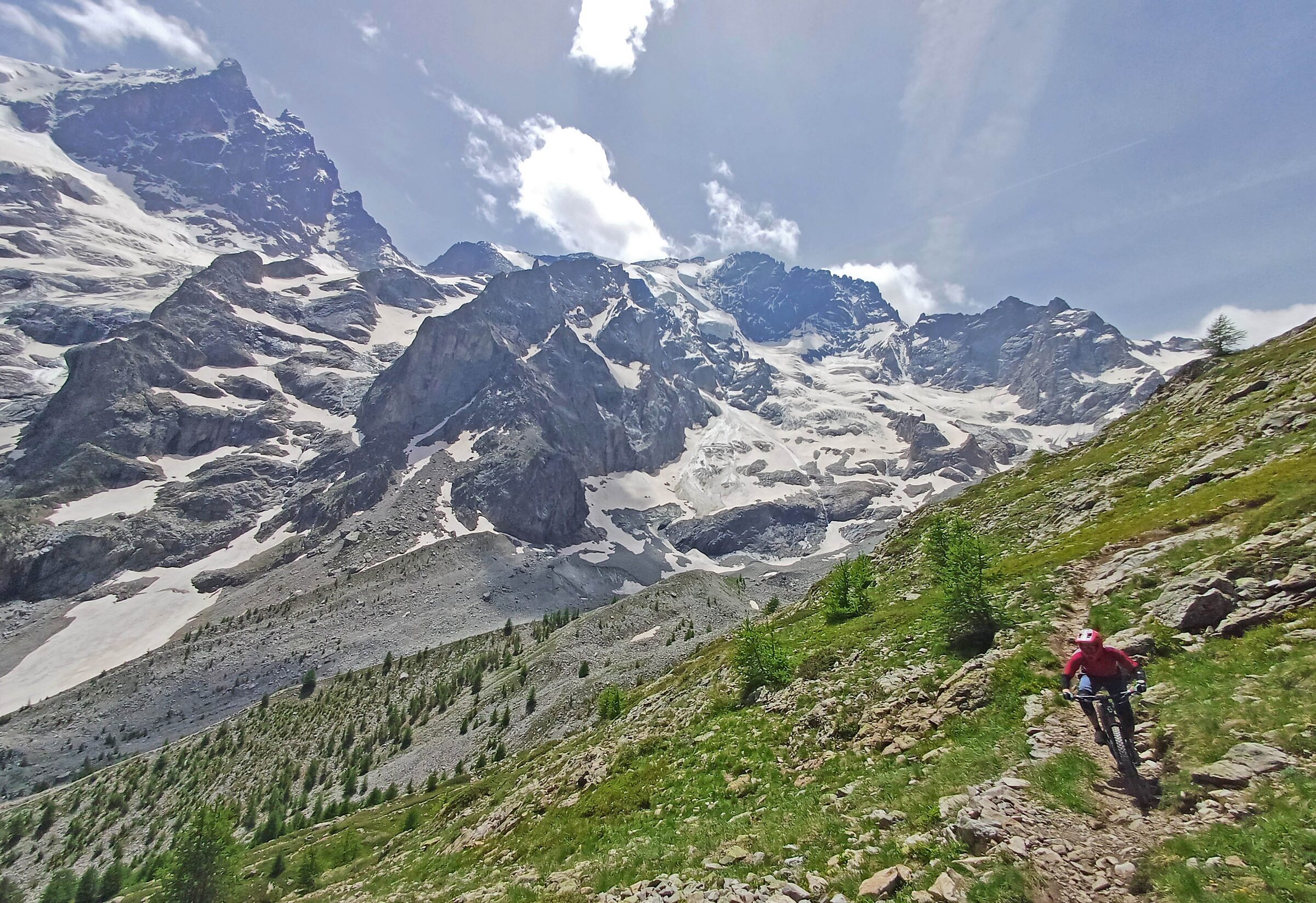 Mountain biker descending a rocky Alpine trail beneath high snowy peaks