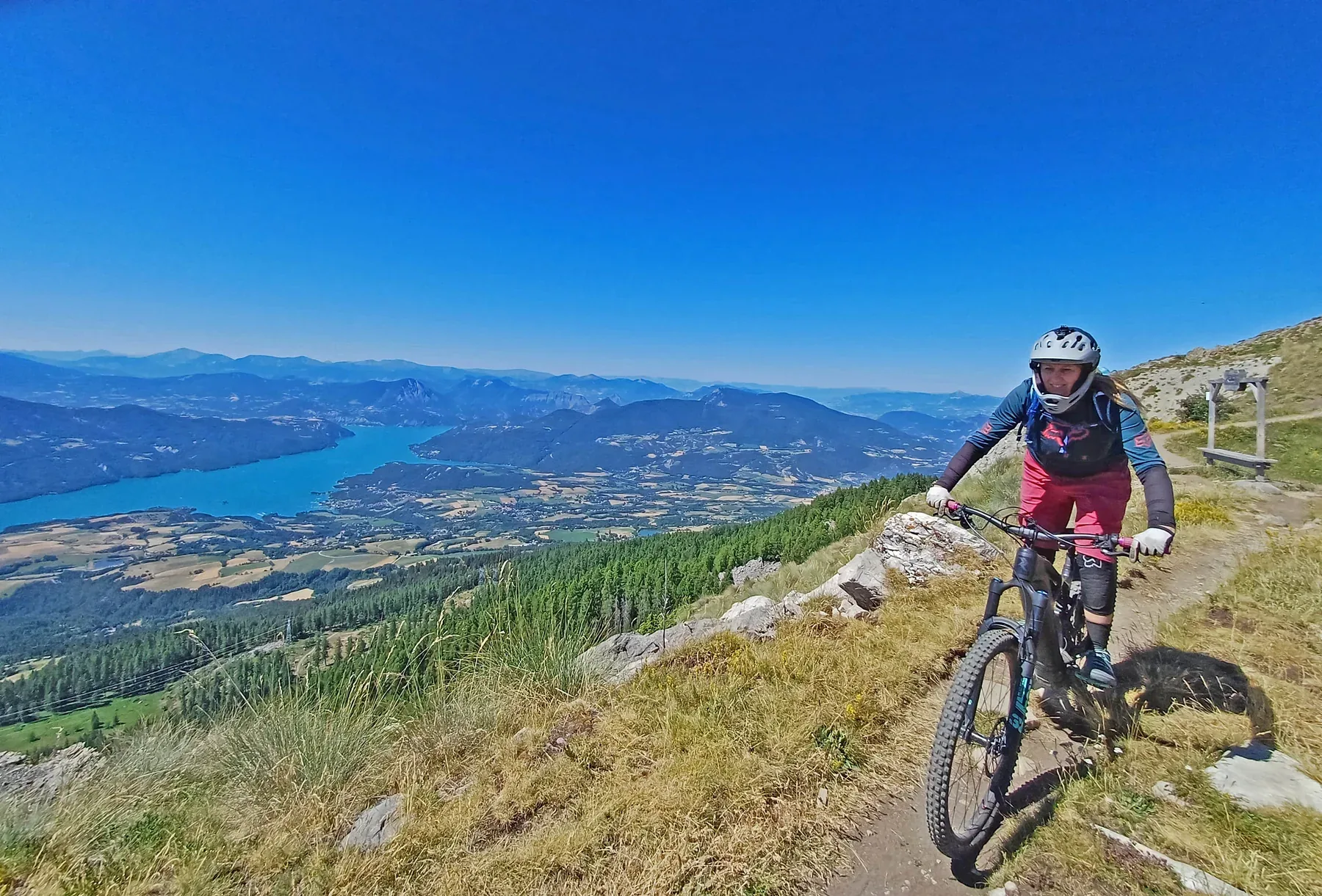 Mountain biker riding a rocky ridge trail above an Alpine lake and valley