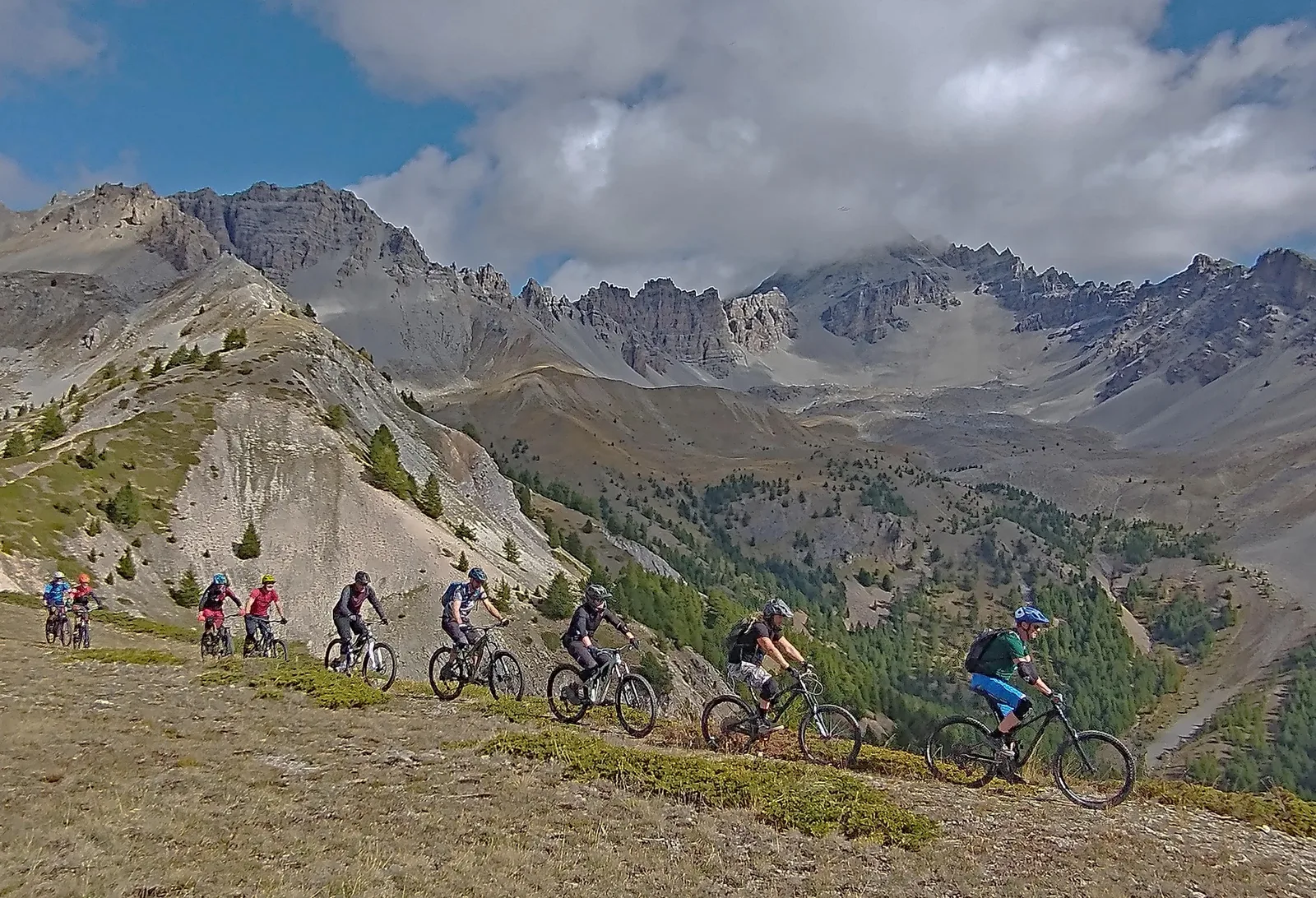 Group of mountain bikers riding a high Alpine traverse beneath cloud-covered peaks