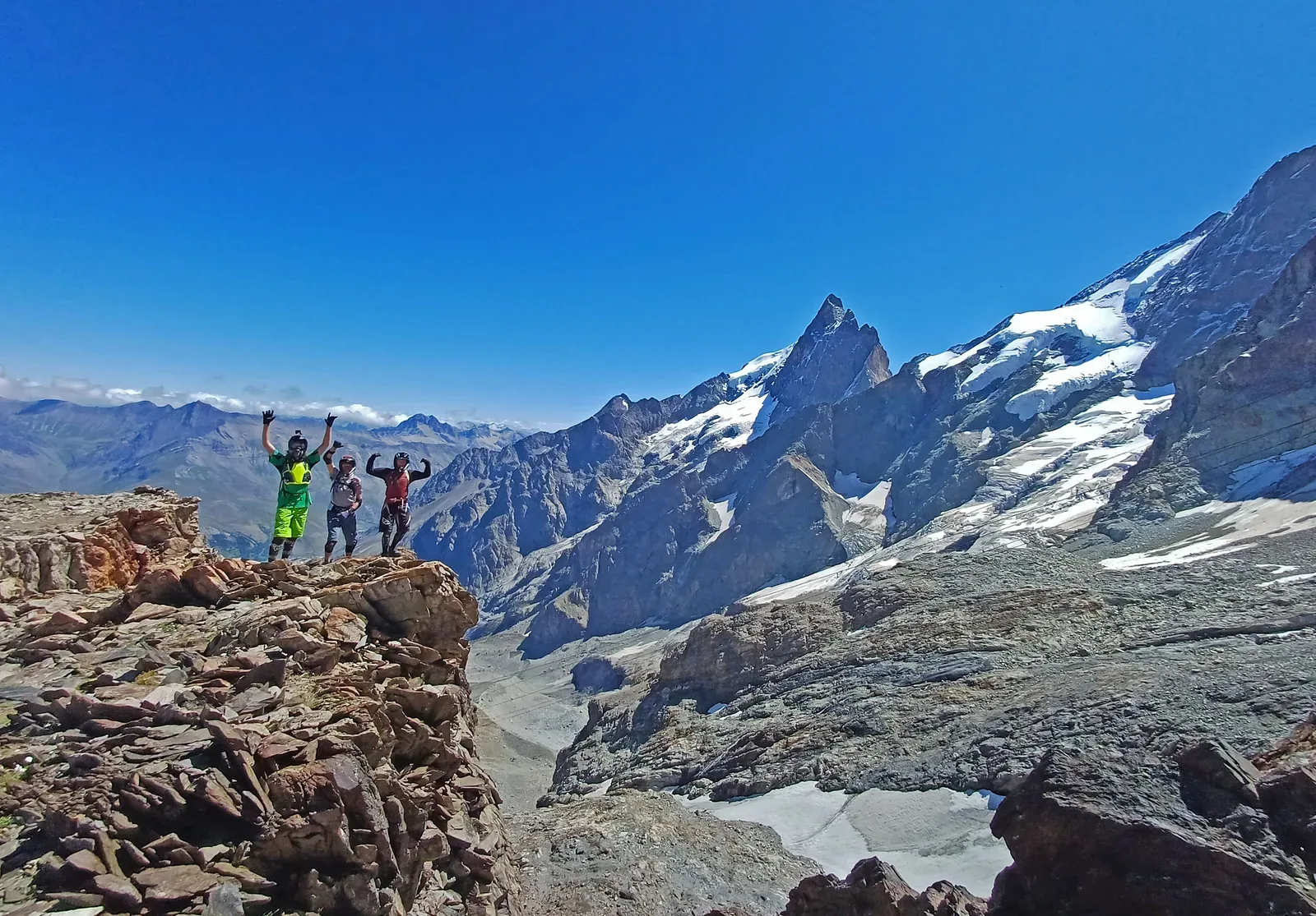Three riders standing above a glaciated Alpine mountain landscape