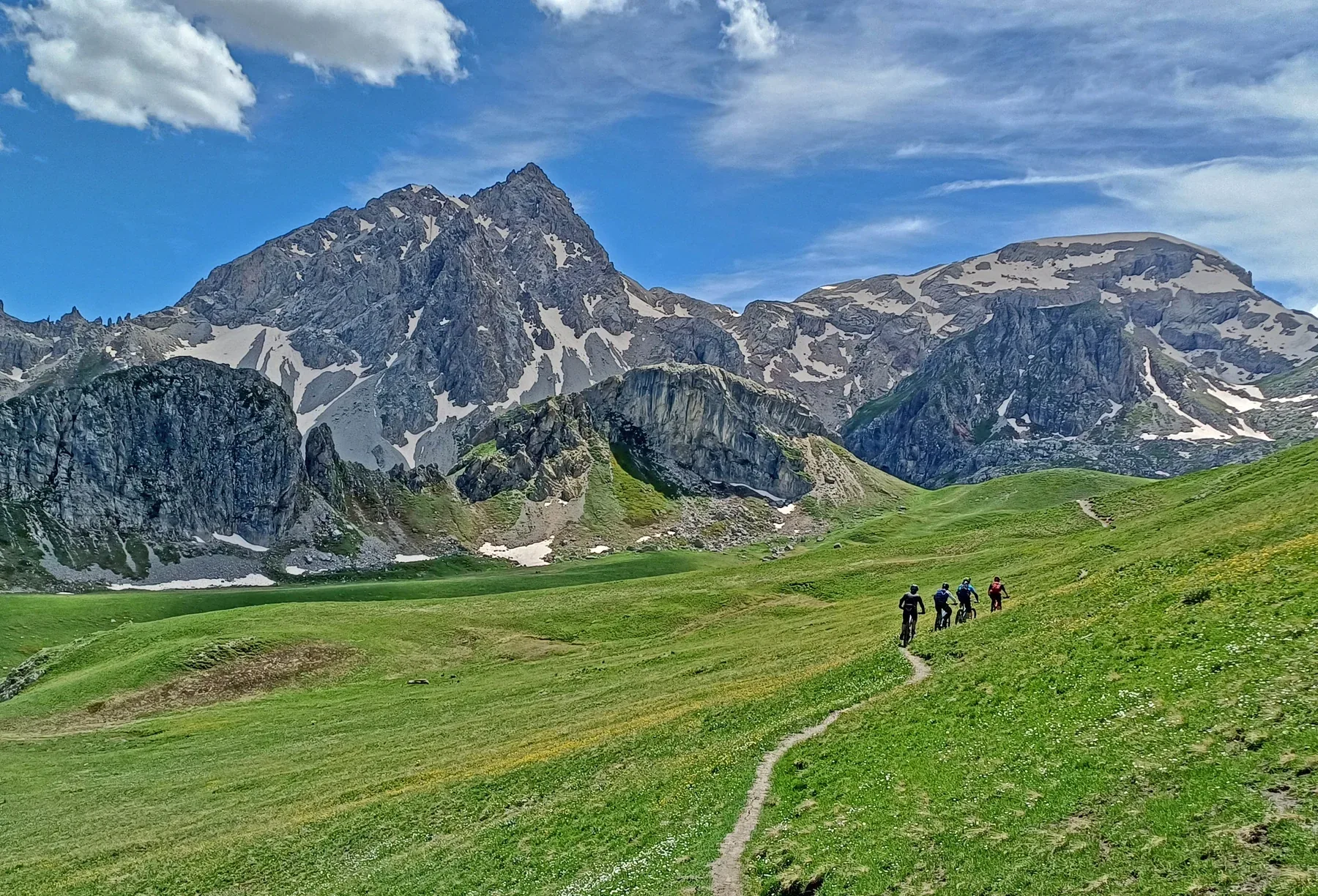 Mountain bikers riding through a high Alpine meadow beneath rugged peaks