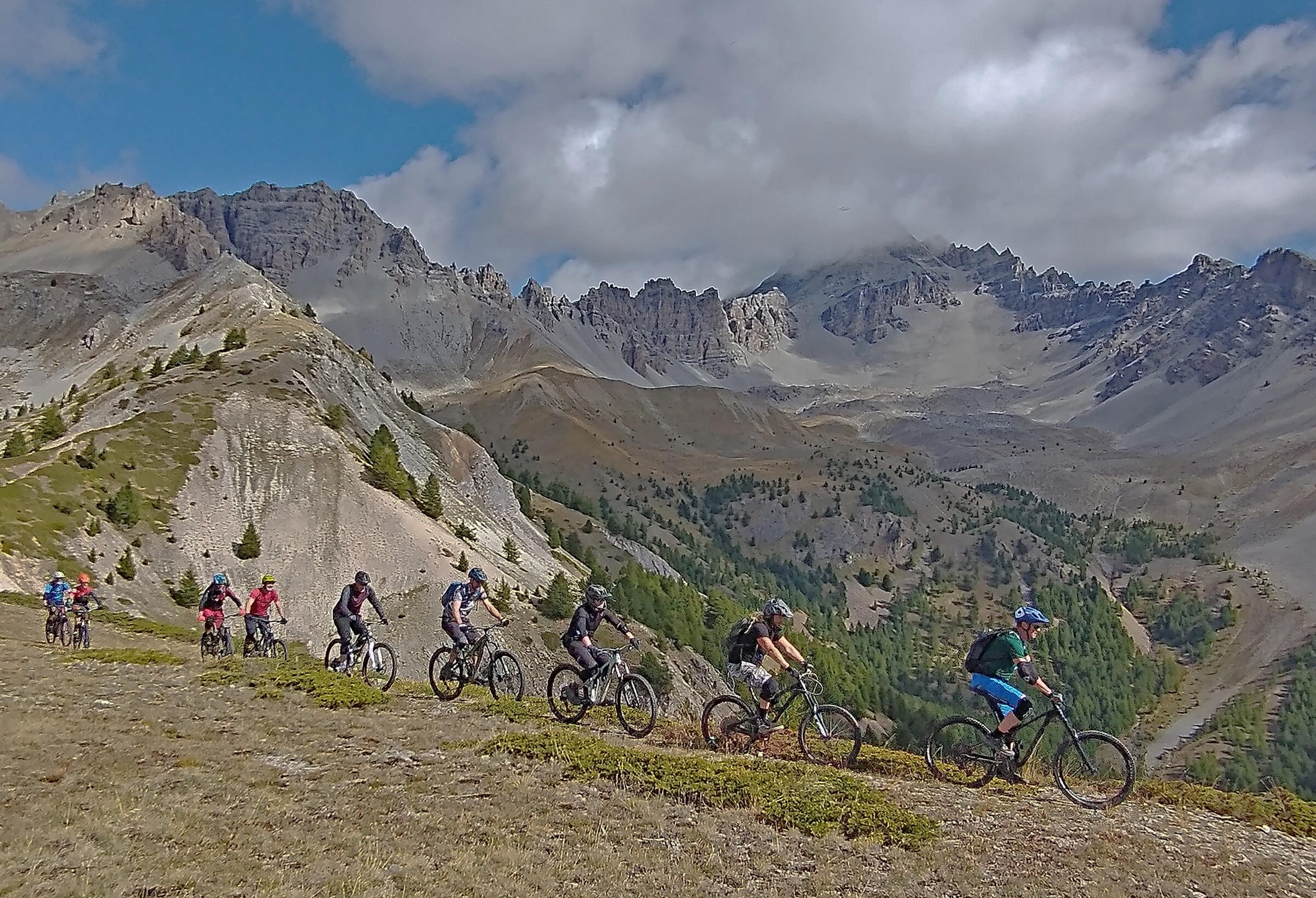 A group of mountain bikers riding a rocky high Alpine slope beneath dramatic clouds