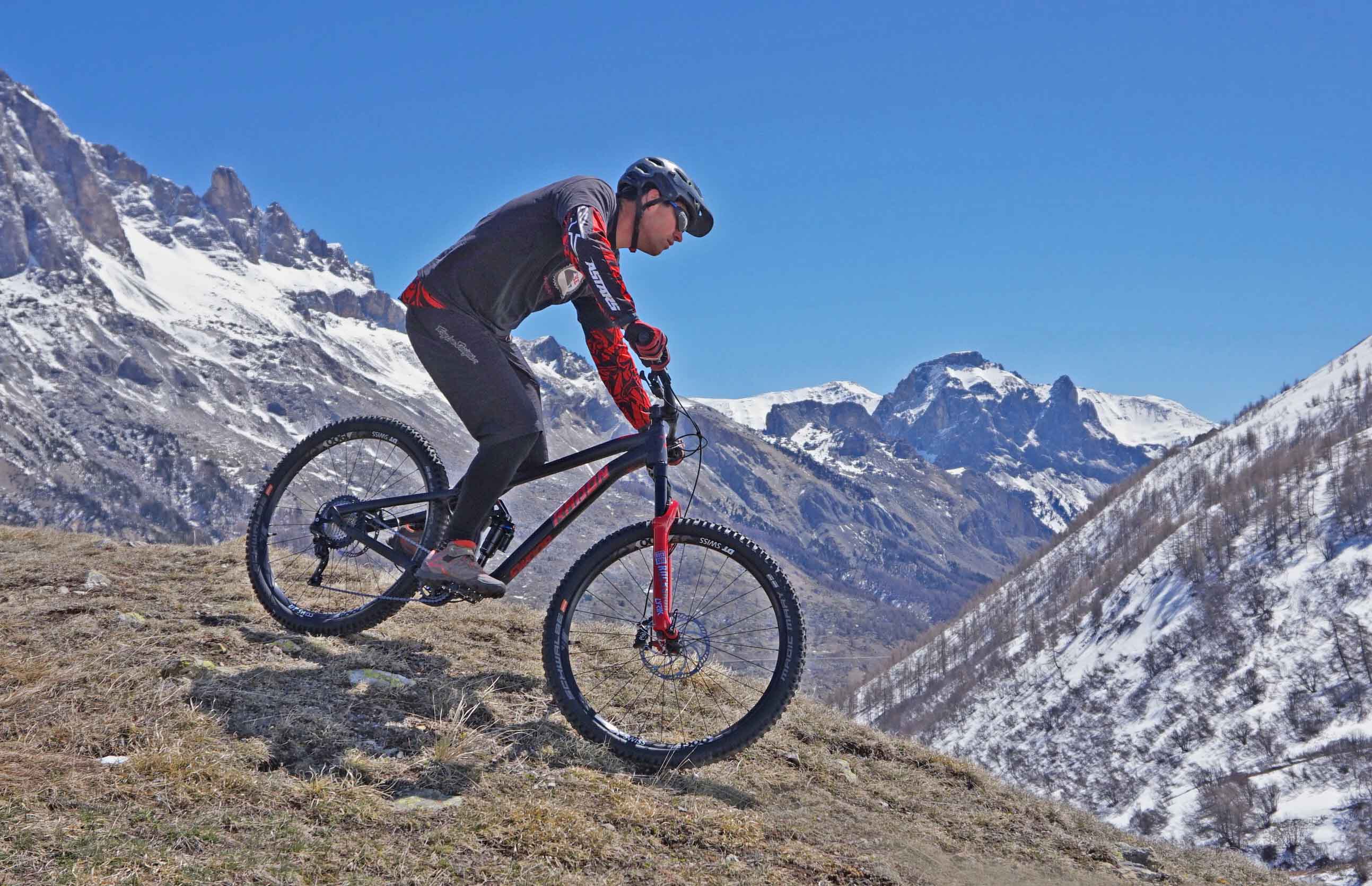 A mountain biker riding an alpine trail beneath snow-covered peaks
